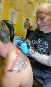 With a smile on his face, Bevan tattoos a back piece on one of his clients. Photo credit: Julie Small. 